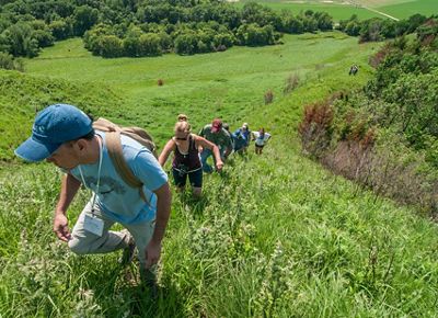 Several people hike up a steep green hill toward the camera.