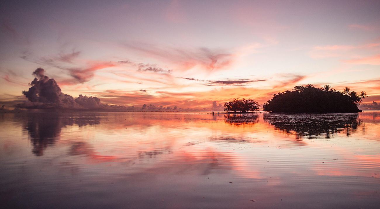 Landscape view of a large flat body of water with a small island; the sky and water are orange at sunset.