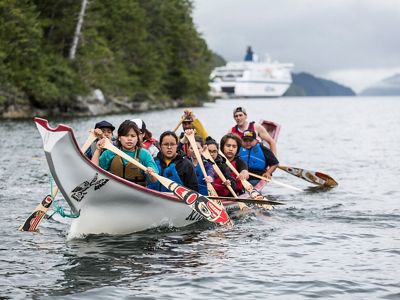 A group of people paddle in a traditional canoe in a waterway in the Great Bear Rainforest.