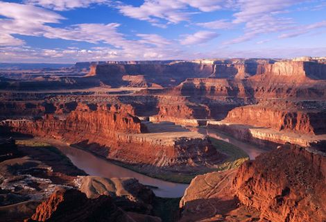 A wide river curves through a landscape of towering mesas that glow red and golden in the sun.