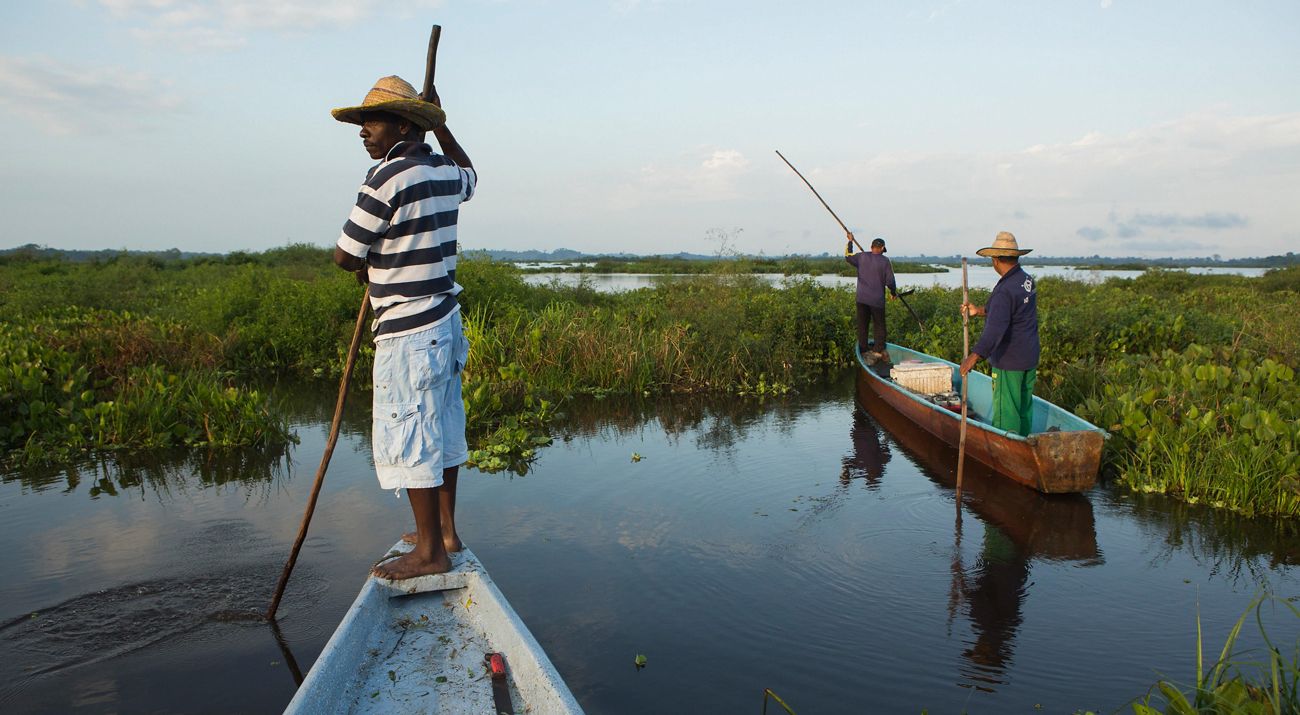Two fishermen in boats navigate the Magdalena River Basin in Colombia.