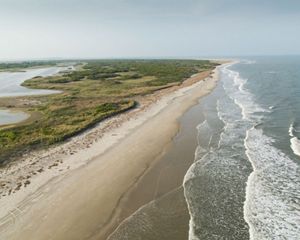 Aerial view of Hog Island, a narrow expanse of sand backed by green scrub and fronted by gently lapping waves.