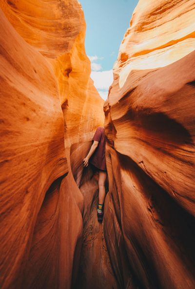 Una mujer camina adentro de una estrecha ranura en un cañón