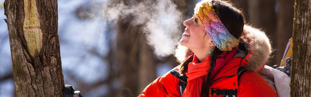 A smiling woman in winter gear outside in cold weather with her breath visible around her head.