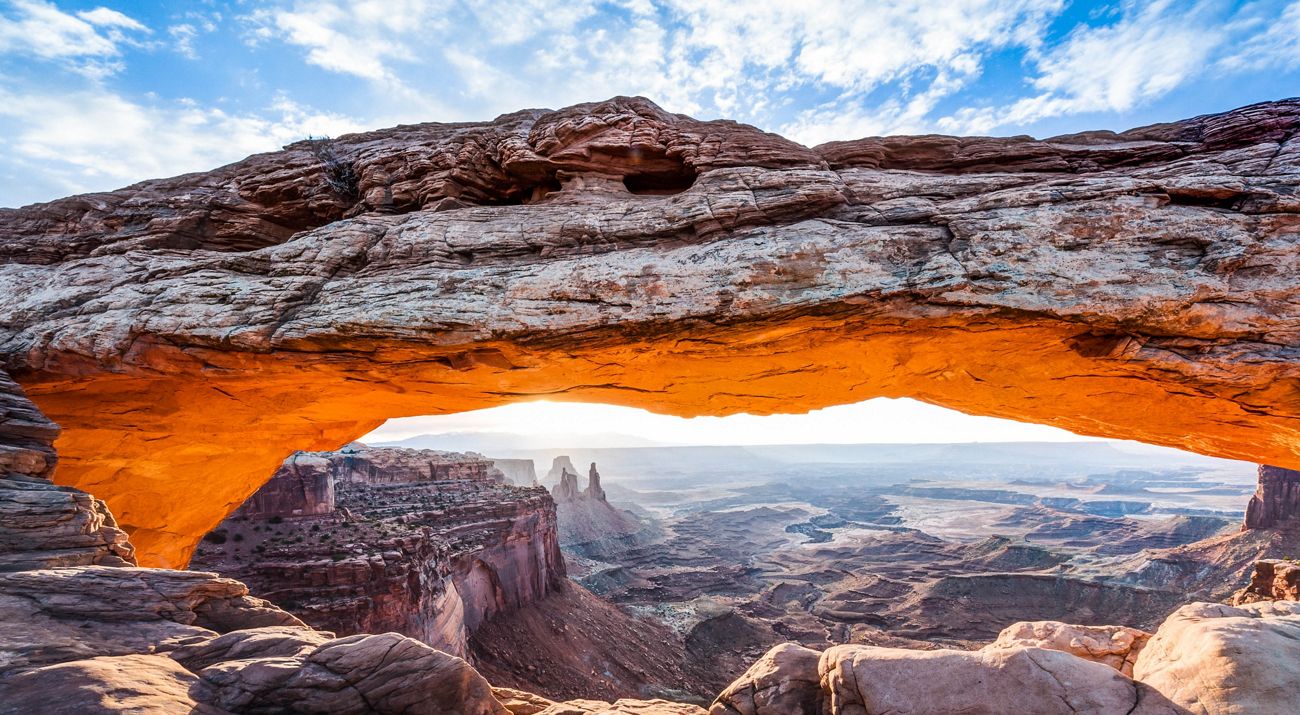 Arched red rock formation in sunrise light with valley in the background.