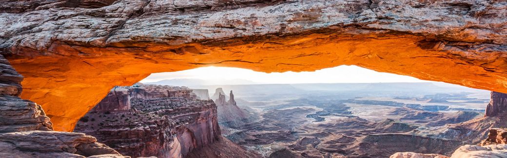 A large stone arch extends in the foreground over a desert landscape in the distance.