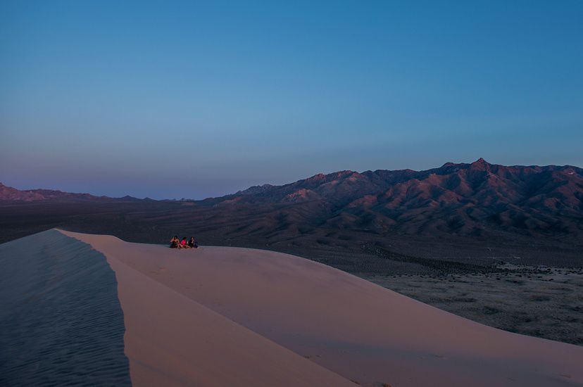 Photo at dusk of California dunes, three people in background sitting on dune. 