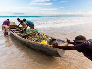 men pushing a small wooden boat filled with fishing nets.
