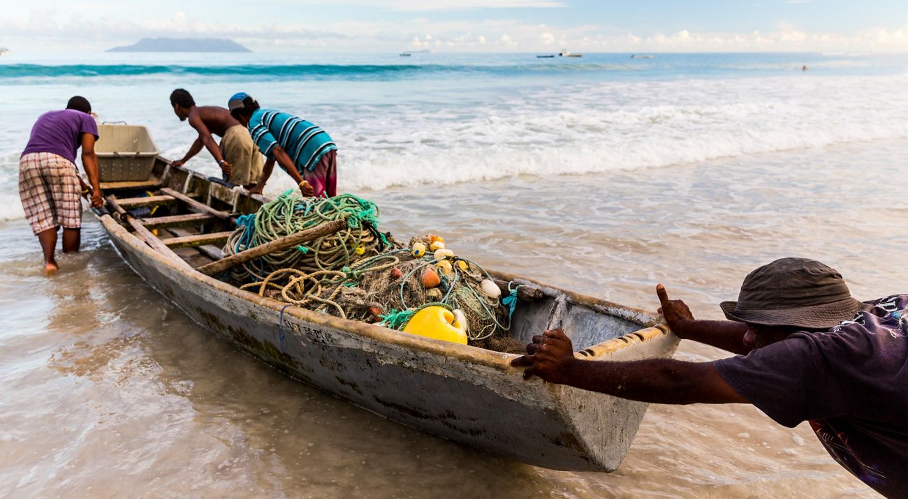 A person pushes a boat with ropes and nets into the water.