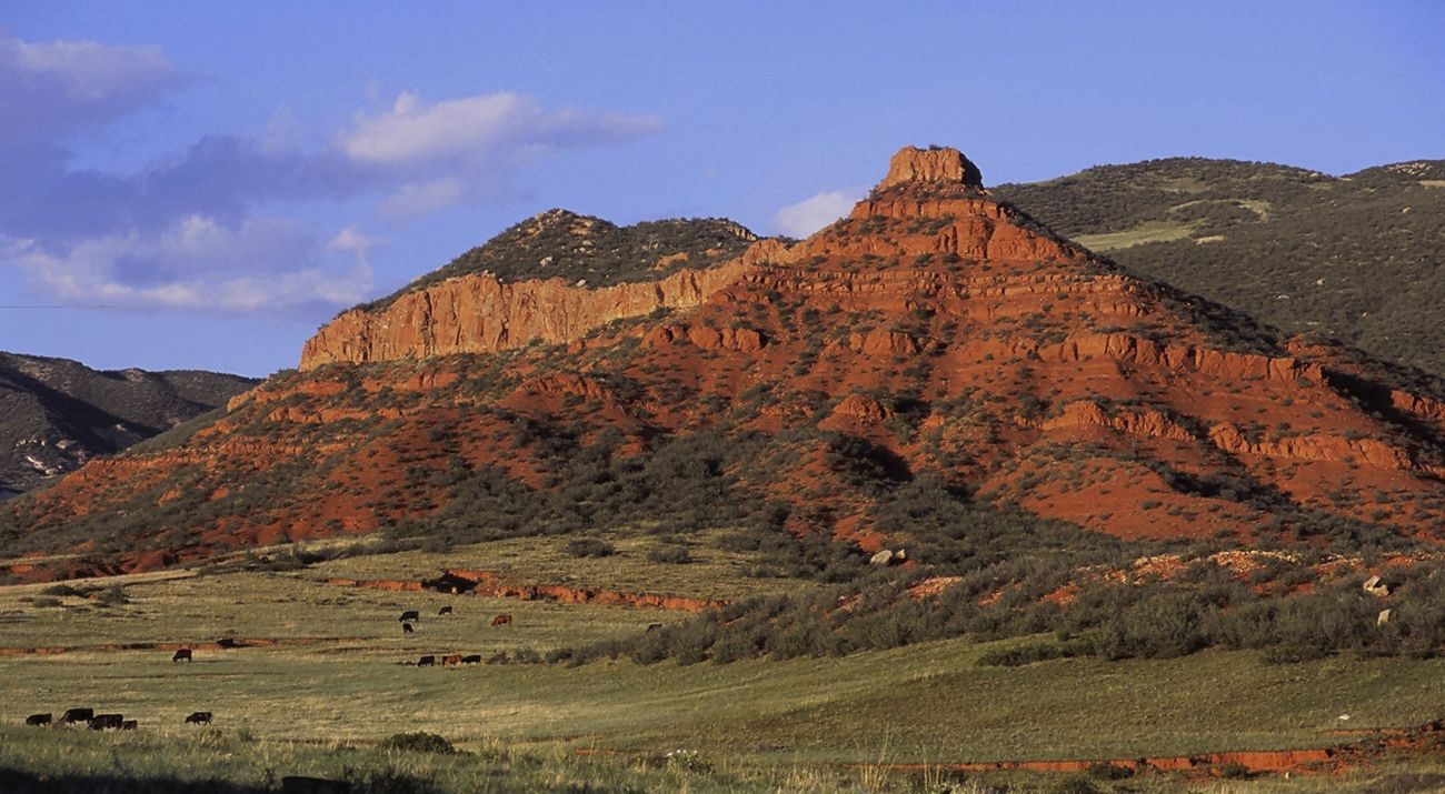 Large red-rock cliffs tower above a rolling green landscape.