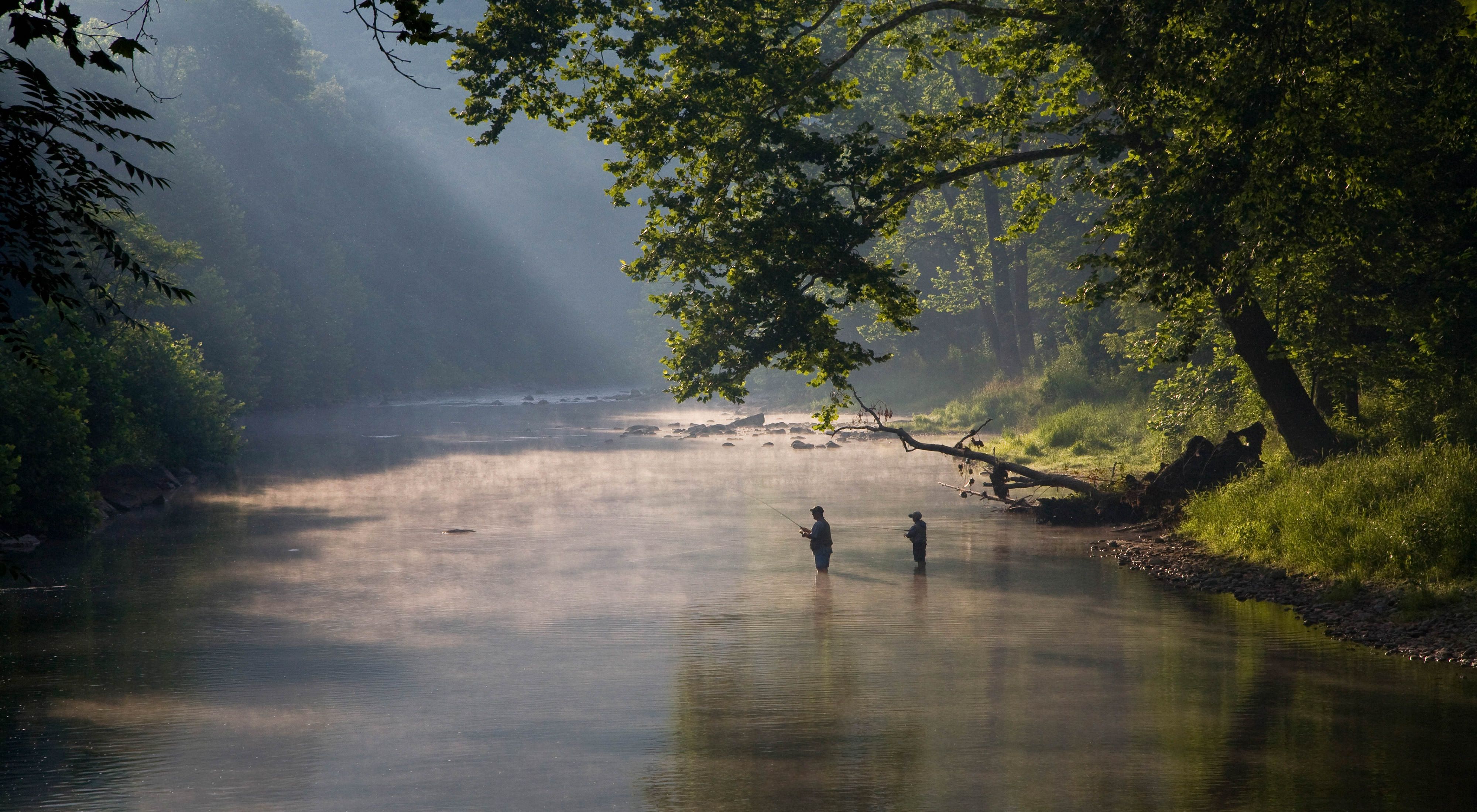 Two people standing in a misty river fly-fishing.