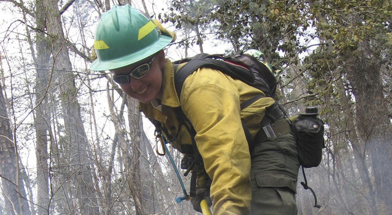 A smiling woman tends to a fire line during a controlled burn.