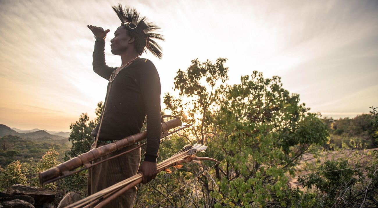 A man with a bow and arrows surveys a valley in Tanzania looking for game.