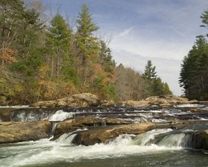 A rocky river flows between two forested banks in autumn.