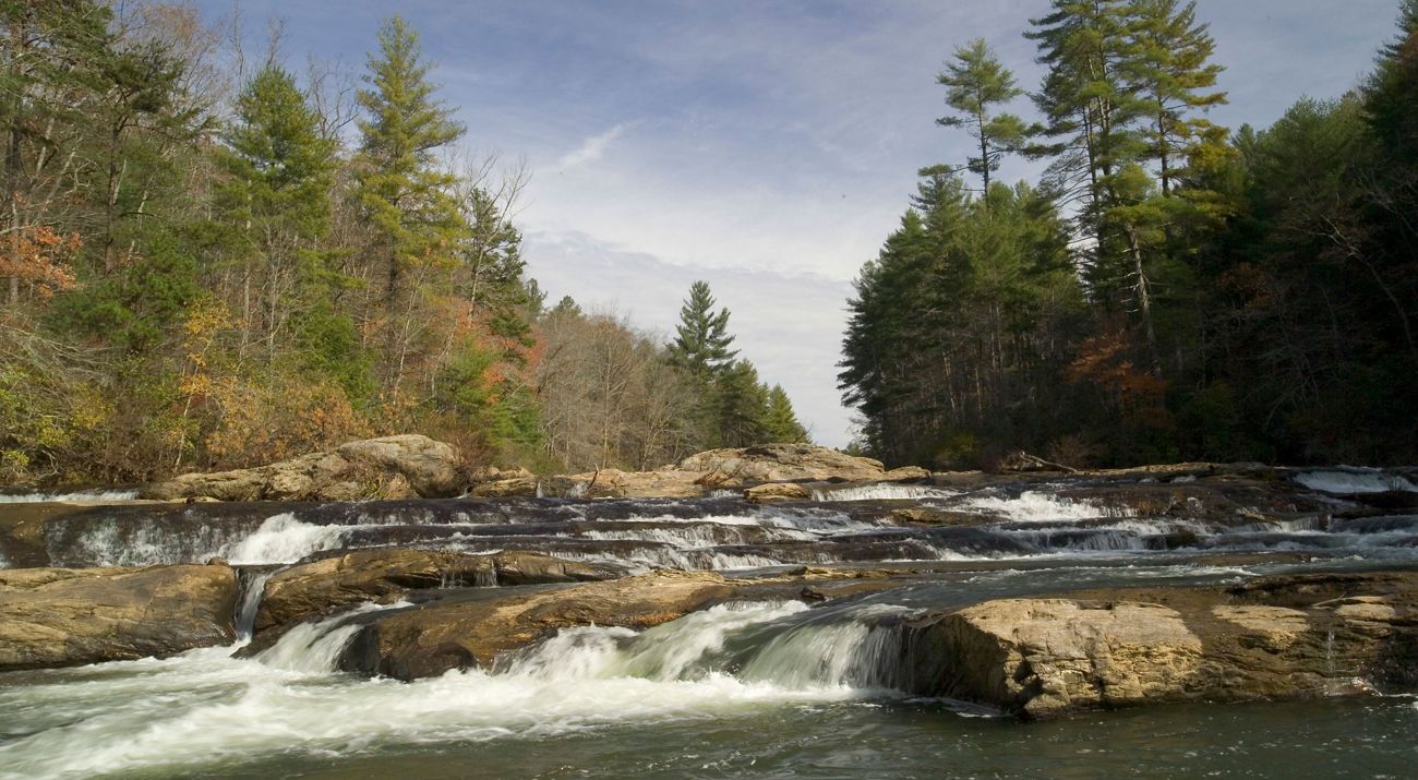 A rocky river flows between two forested banks in autumn.