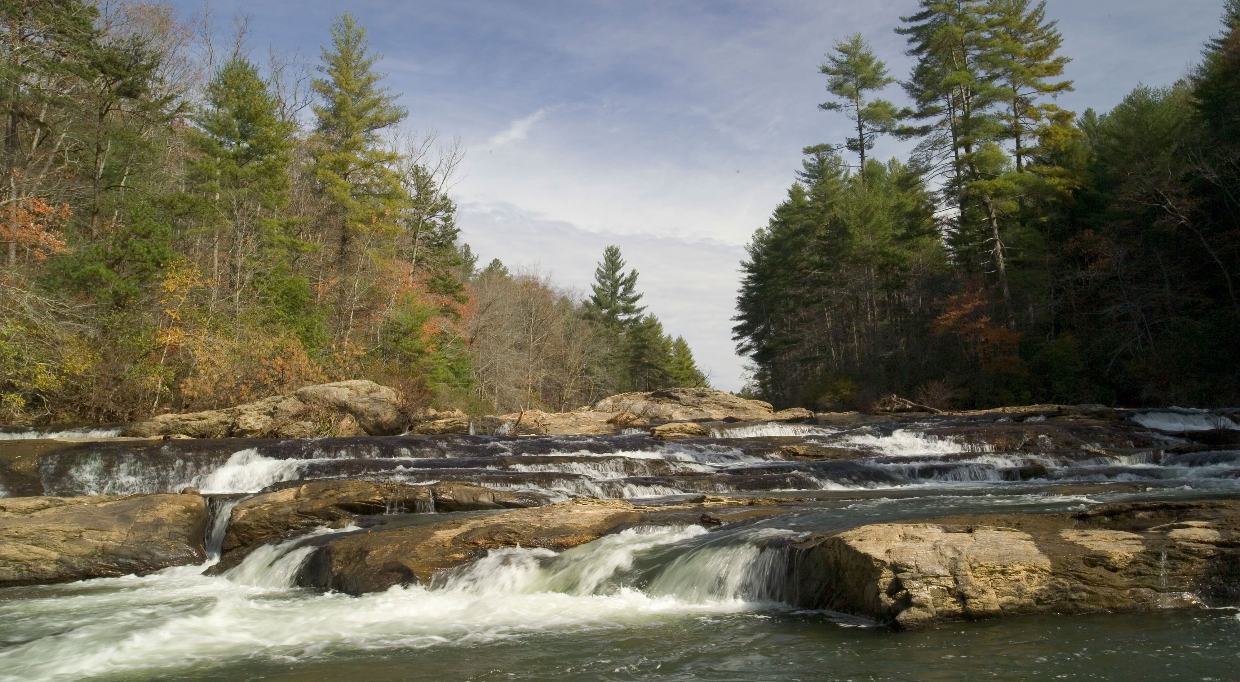 A rocky river flows between two forested banks in Autum
