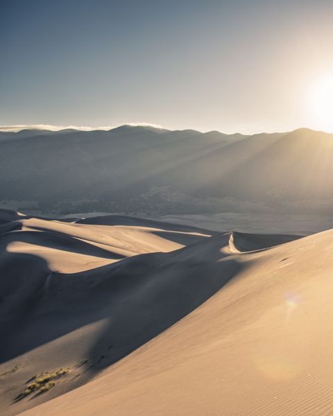 A silhouette of a person hiking along golden sand dunes at Great Sand Dunes National Park. 
