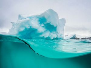 A crystal blue glacier sits on top of ocean water.