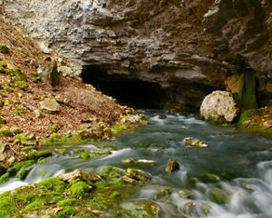 A rocky save opening with water flowing from it.