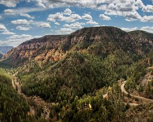 Landscape of a mountain that is full of large, green ponderosa pine pine trees with a blue sky and clouds above it.