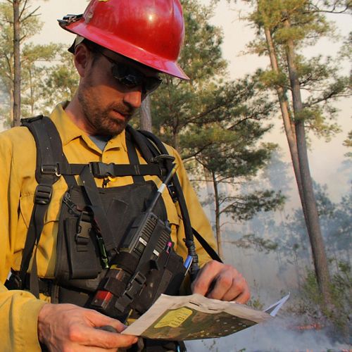 Sam Lindblom headshot. A man wearing yellow fire gear and a red hard hat.