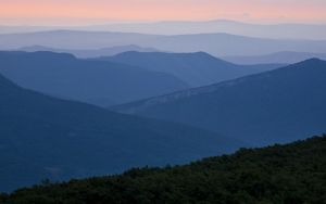 Blue mountain ridgetops roll across the landscape ending at the pink horizon.