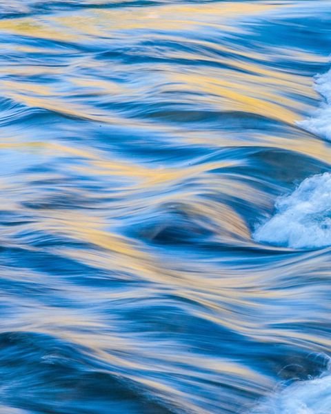 A close-up of flowing water with yellow sunlight highlighting the water's surface. 