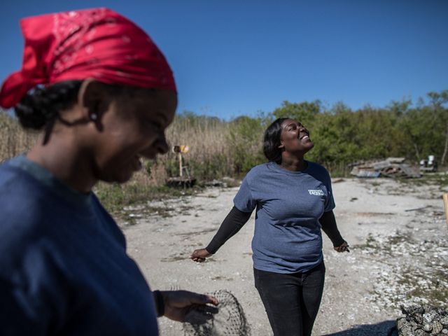 Conservation Corps member Dee Dee, 21, shares a laugh with her colleague, Myesha Campbell, 20, while creating natural seawall barriers using old oyster shells.