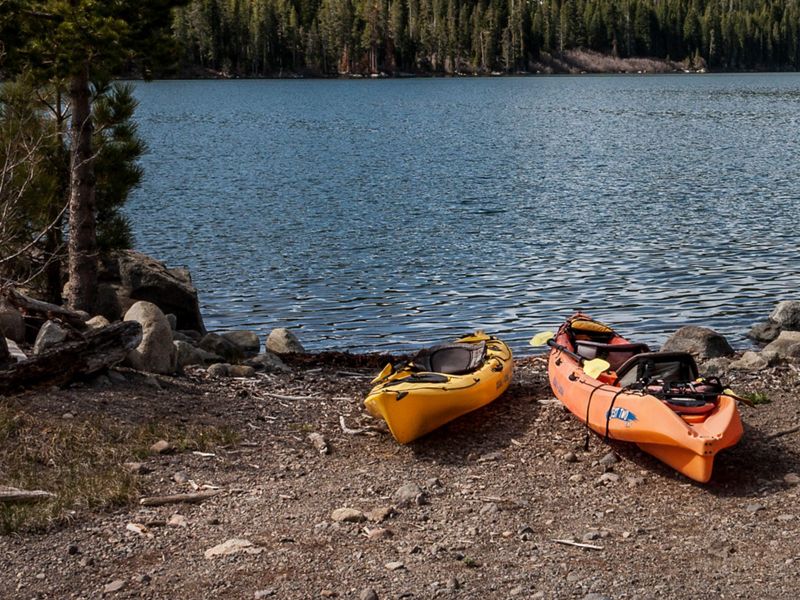 Two kayaks sit at the side of a lake.