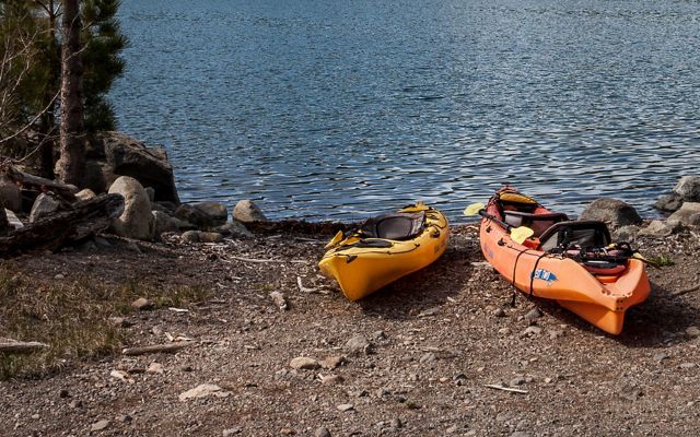 Two kayaks sit at the side of a lake.