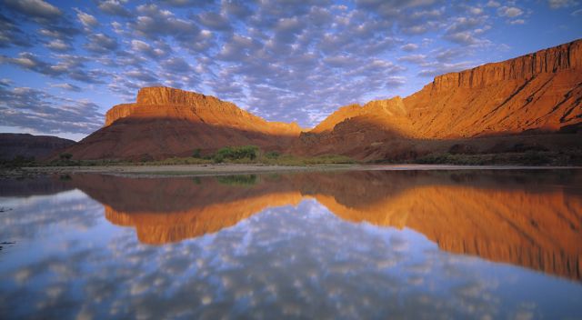 Buttermilk clouds and red cliffs reflected in a river.