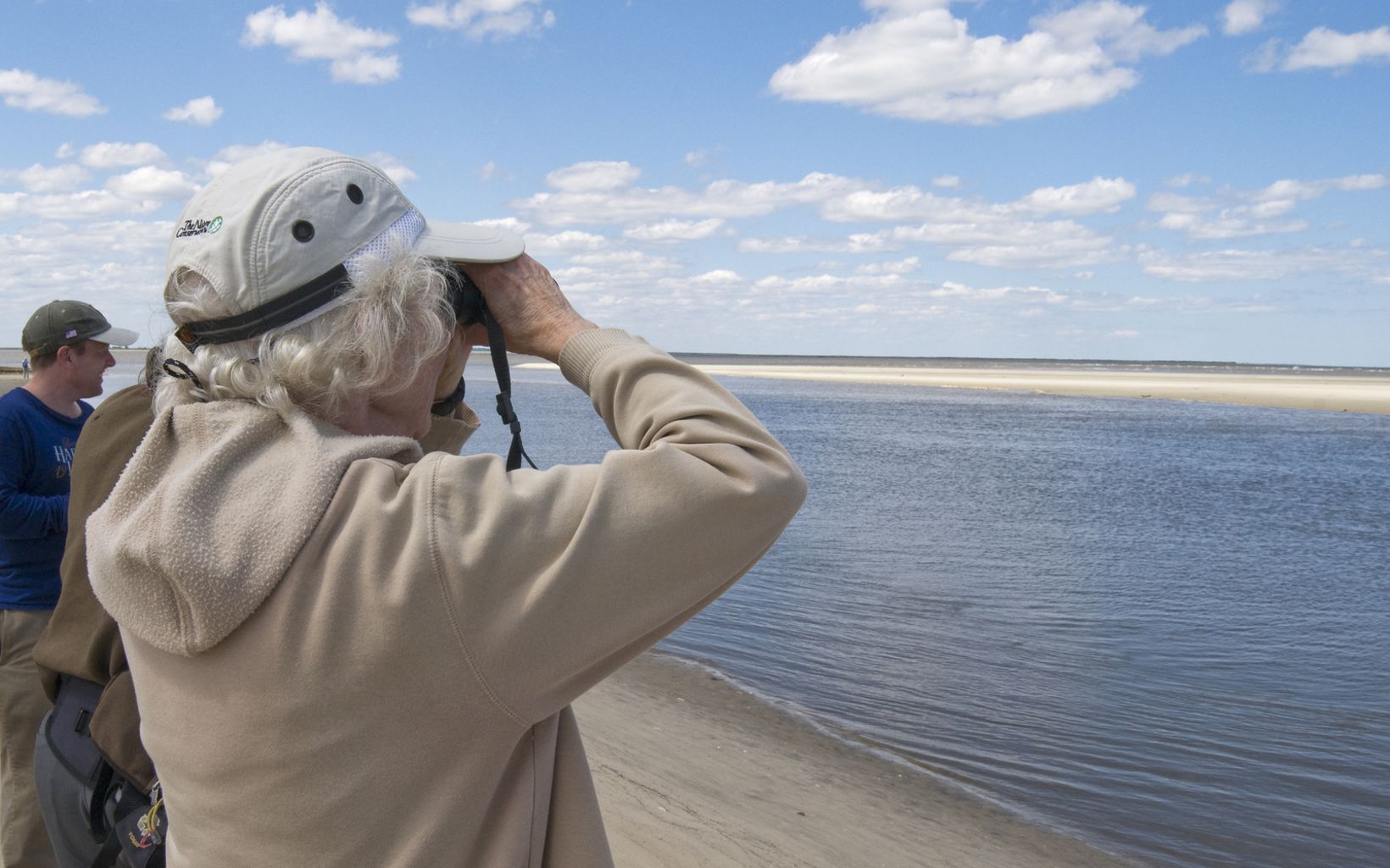 Three people stand along the tidal shores of Little St. Simons Island looking for birds and other wildlife.
