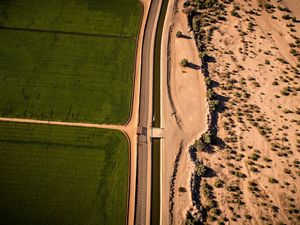 An irrigation canal divides green U.S. farmland and the dry Sonoran desert by the USA/Mexican border.