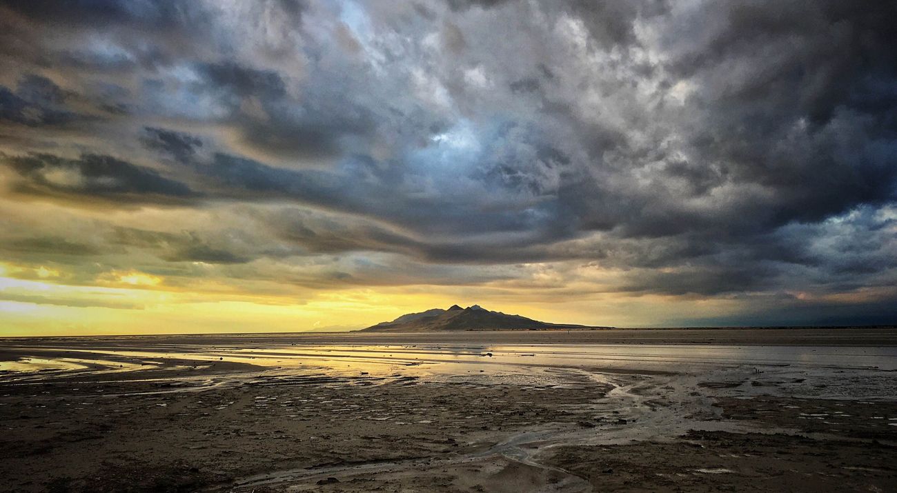 Shallow water in the great salt lake under dramatic cloudy skies with a hill in the distance.
