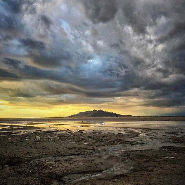 Shallow water in the Great Salt Lake under dramatic cloudy skies with a hill in the distance.