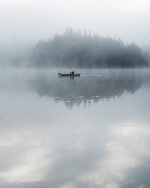 A person sits in a canoe on calm waters.