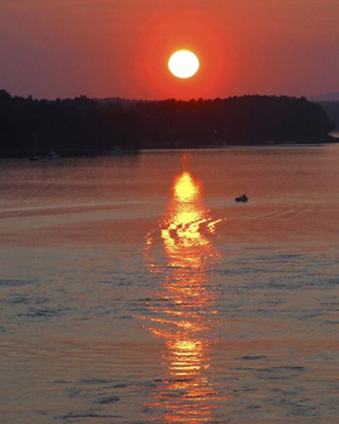 A boat chugs through a bay at sunset.