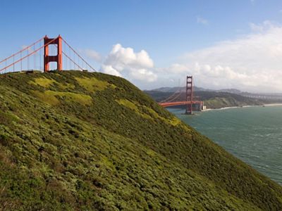 Golden Gate Bridge viewed from a distance with a green, undeveloped hillside in the foreground.