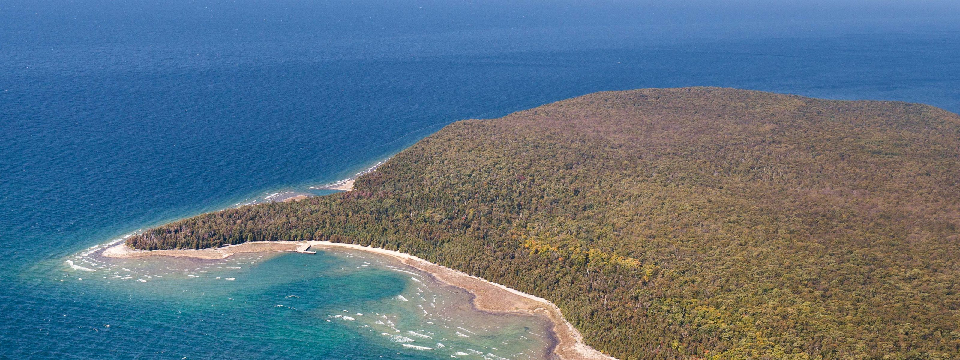 Aerial view of a peninsula covered in dense forest and a blue ocean surrounding it.