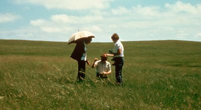 Three people looking at grass in the prairie.