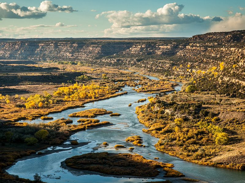 A wide river is running through a landscape with shrubs and mesas in the background.
