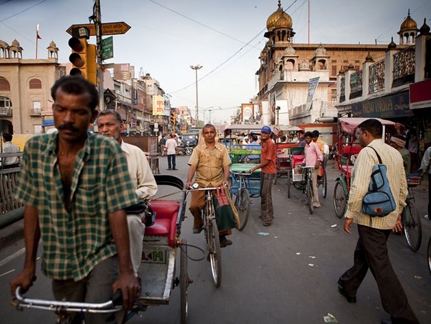 Dozens of people, rickshaws, and motor vehicles crowd a street in New Delhi, India.