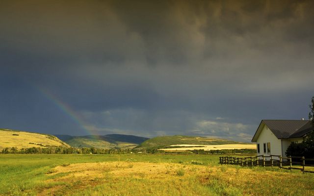 A scenic shot of TNC's Carpenter Ranch; a house with a rail fence sits in an expansive field with a rainbow over the hills in the distance. 