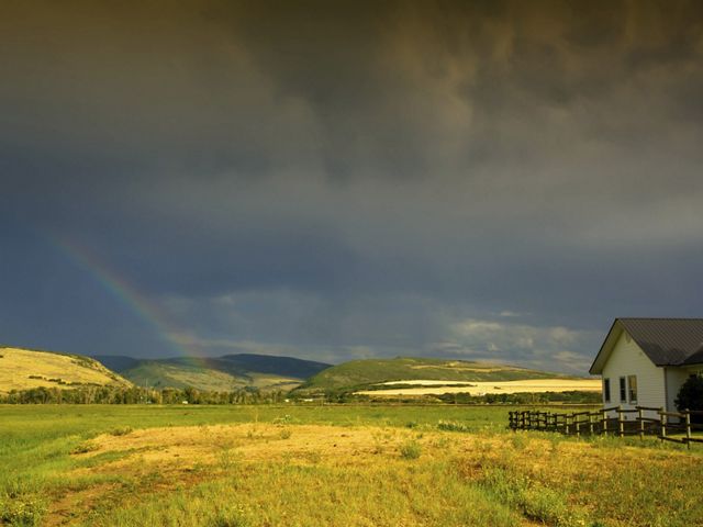 A ranch house on vast grasslands with a stormy sky and a rainbow in the distance.