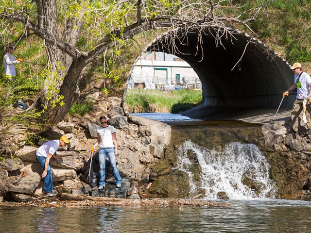 Volunteers pick up trash using grabbers, while standing near a stream and a large culvert.