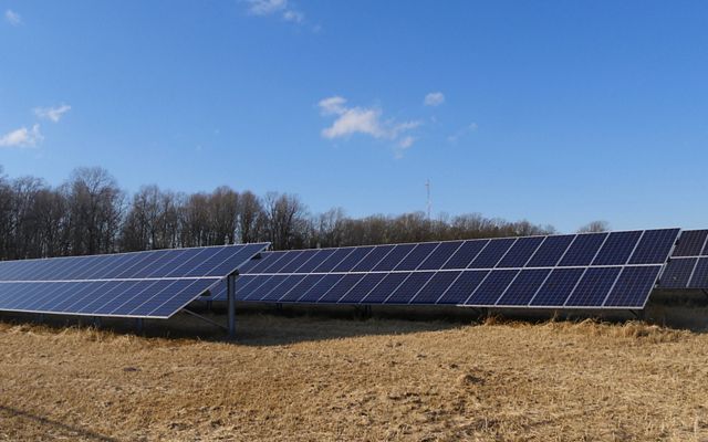 Three rows of solar panels sit in an open field.