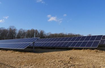 Three rows of solar panels sit in an open field.