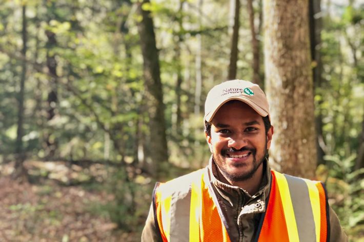 Pabodha Galgamuwa headshot. A smiling man wearing a ballcap and orange and yellow reflective vest stands in a forest.