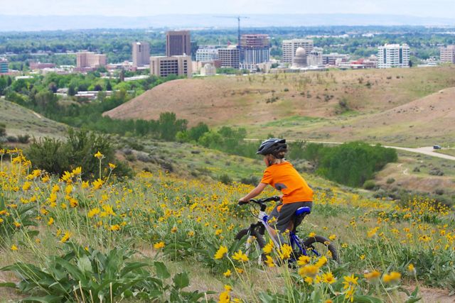 A young child rides a bike on a dirt trail with the City of Boise in the distance. 