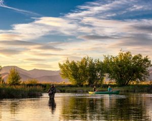 Angler and couple in a canoe floating down a river at sunset.